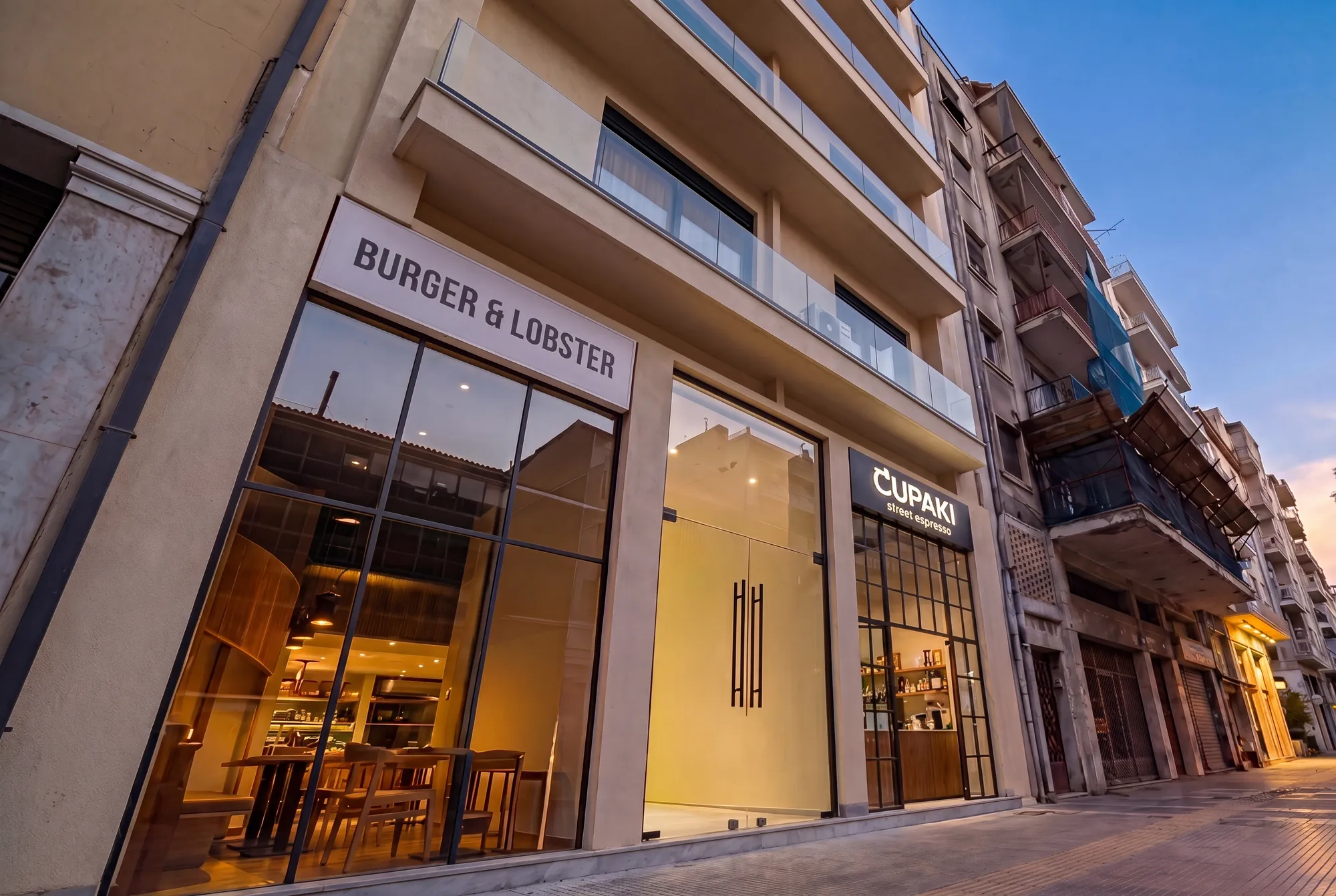 ORMOS Piraeus, the ground floor of ORMOS Piraeus at dusk, the entrance between the lit shopfronts