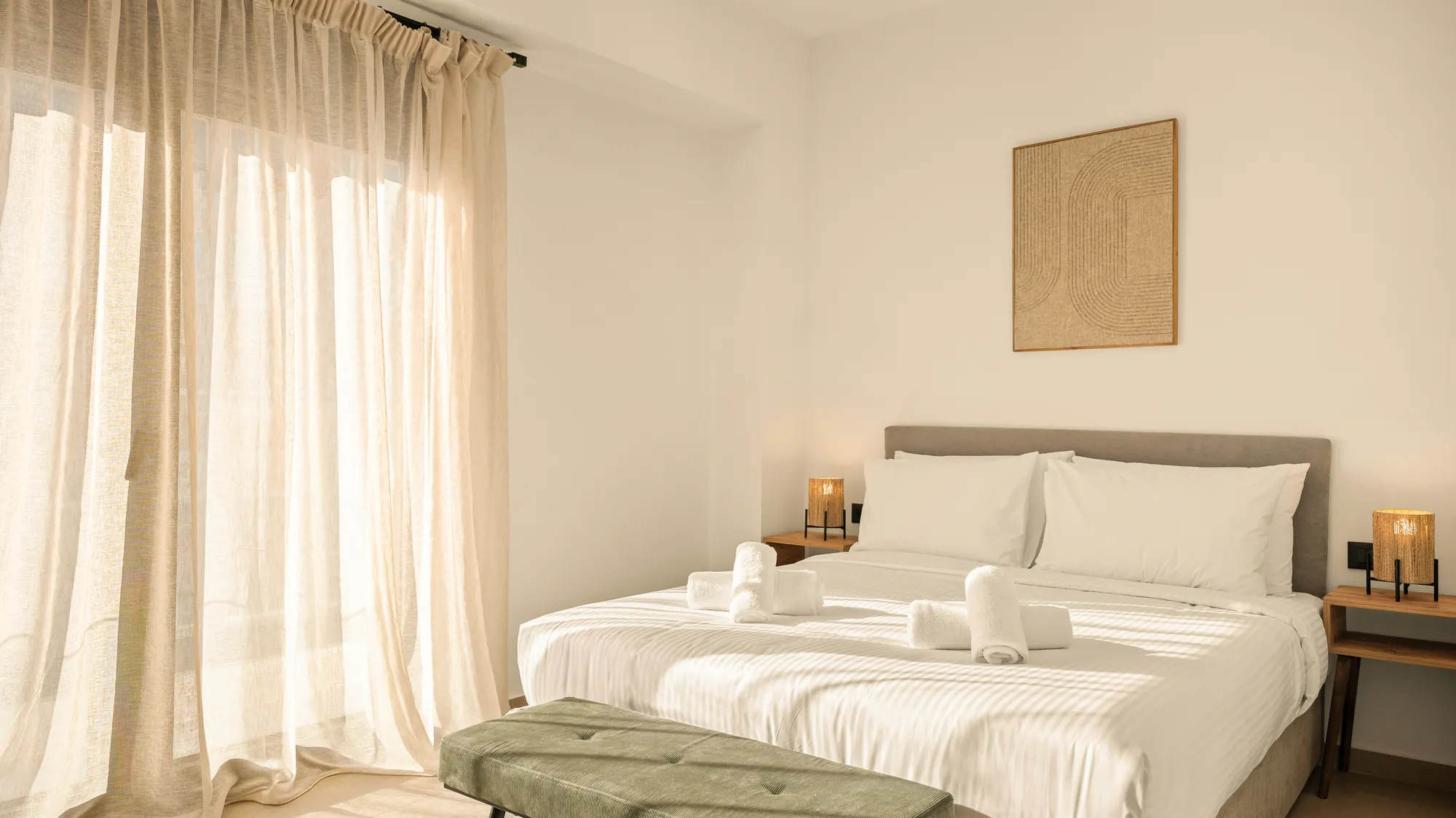 ORMOS Piraeus, a room with linen curtains, the bed made and a green bench at its foot