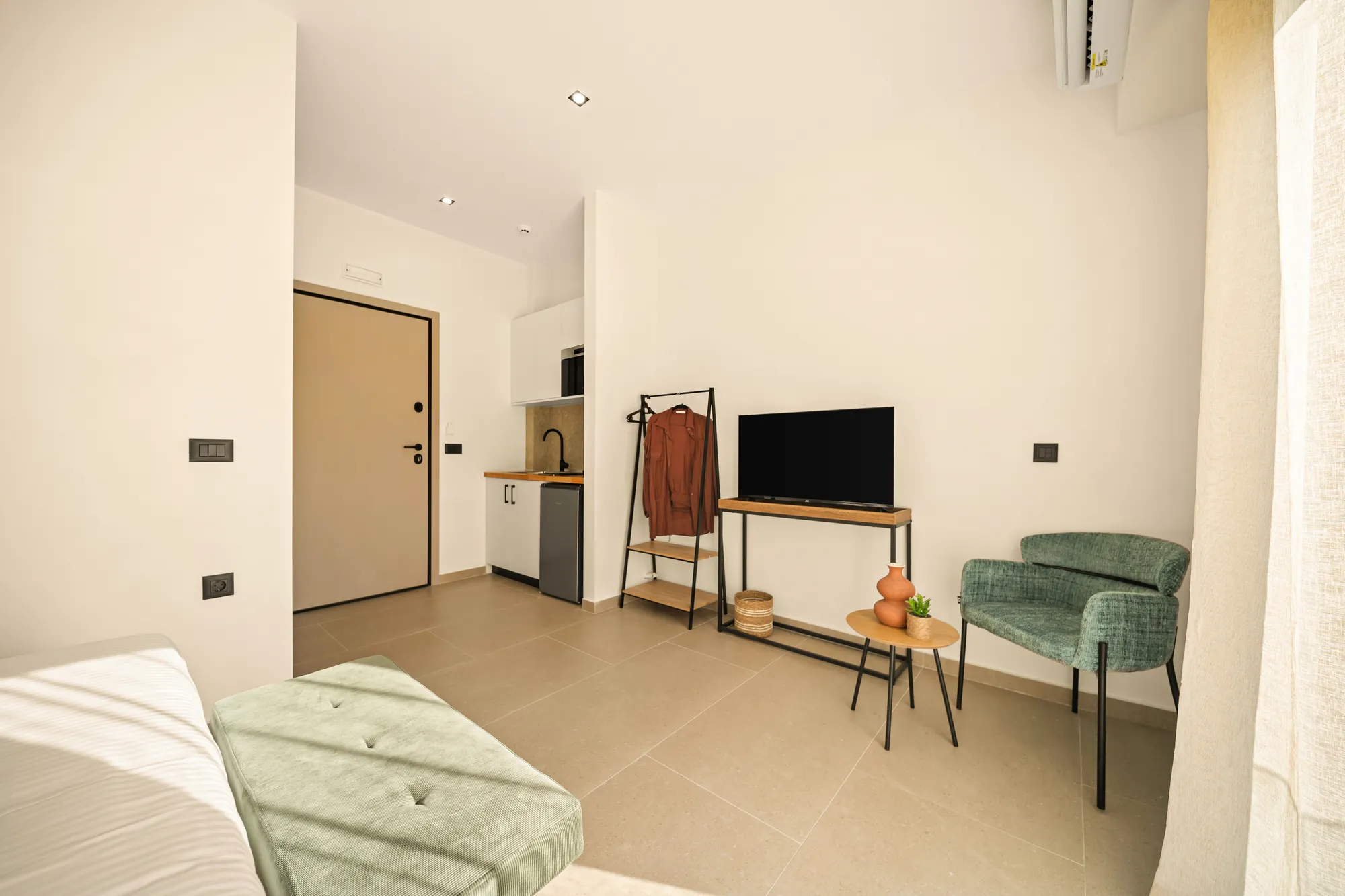 ORMOS Piraeus, the entrance door, the kitchenette and the armchair seen from the bed