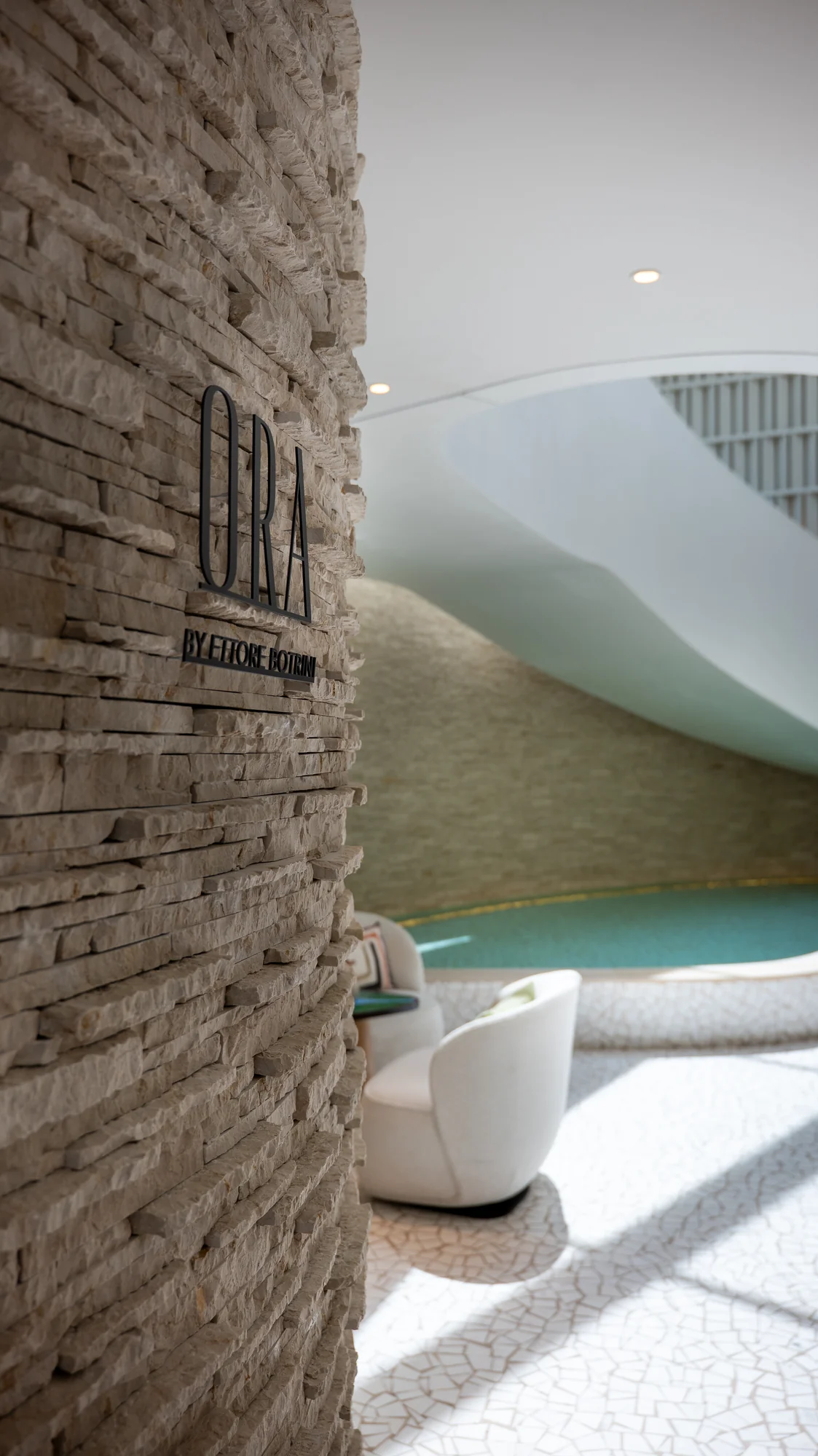One&Only Aesthesis, a curved stone wall beside the reflecting water feature