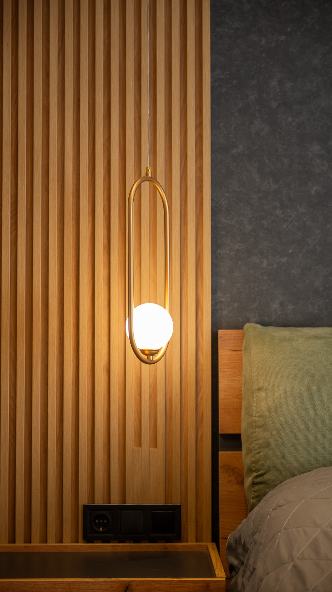 A&K Chorothetisis, brass oval pendant lit against oak slat wall meeting grey felt headboard
