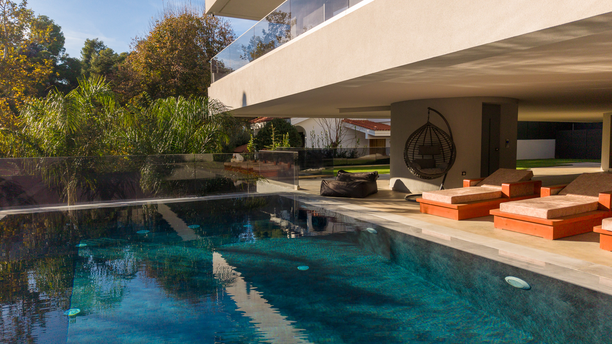Villa Bond, pool with hanging chair and orange loungers at midday